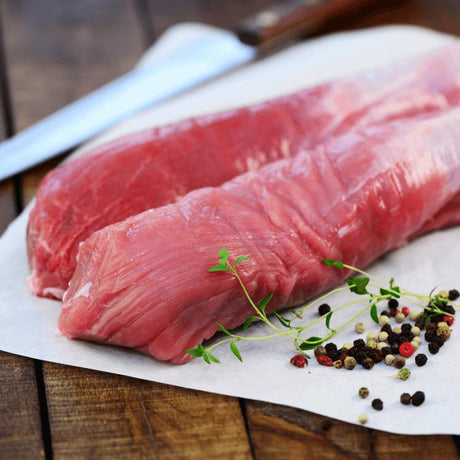 Rohes Schweinefilet auf einer schwarzen Platte, neben frischen Kräutern und Gewürzen für die Zubereitung