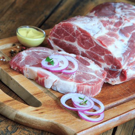 Rohes Schweinenackenstück auf einer holz Platte, flankiert von aromatischen Zwiebeln und Sauce